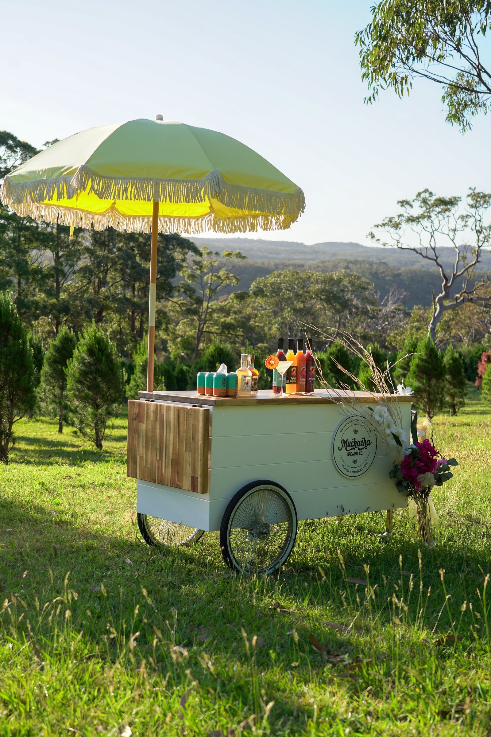 Vintage-style cart with drinks under a yellow umbrella in a scenic outdoor setting