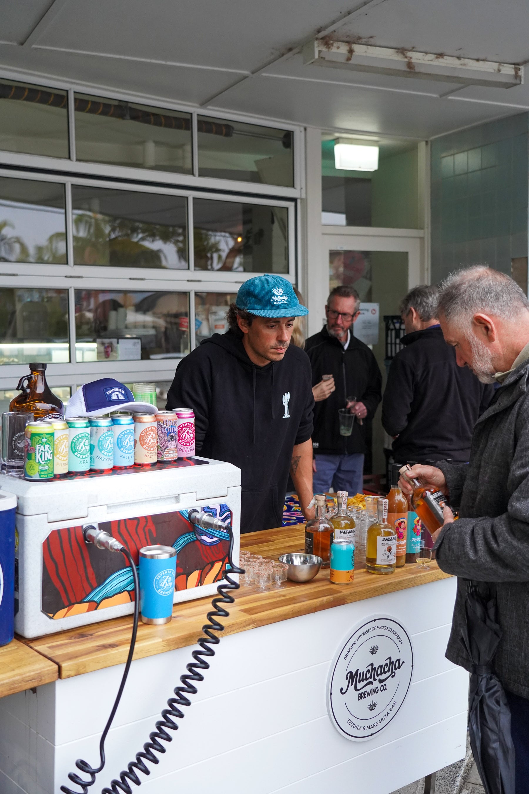 Man behind a counter selling drinks to customers in an outdoor setting. Margarita Tasting