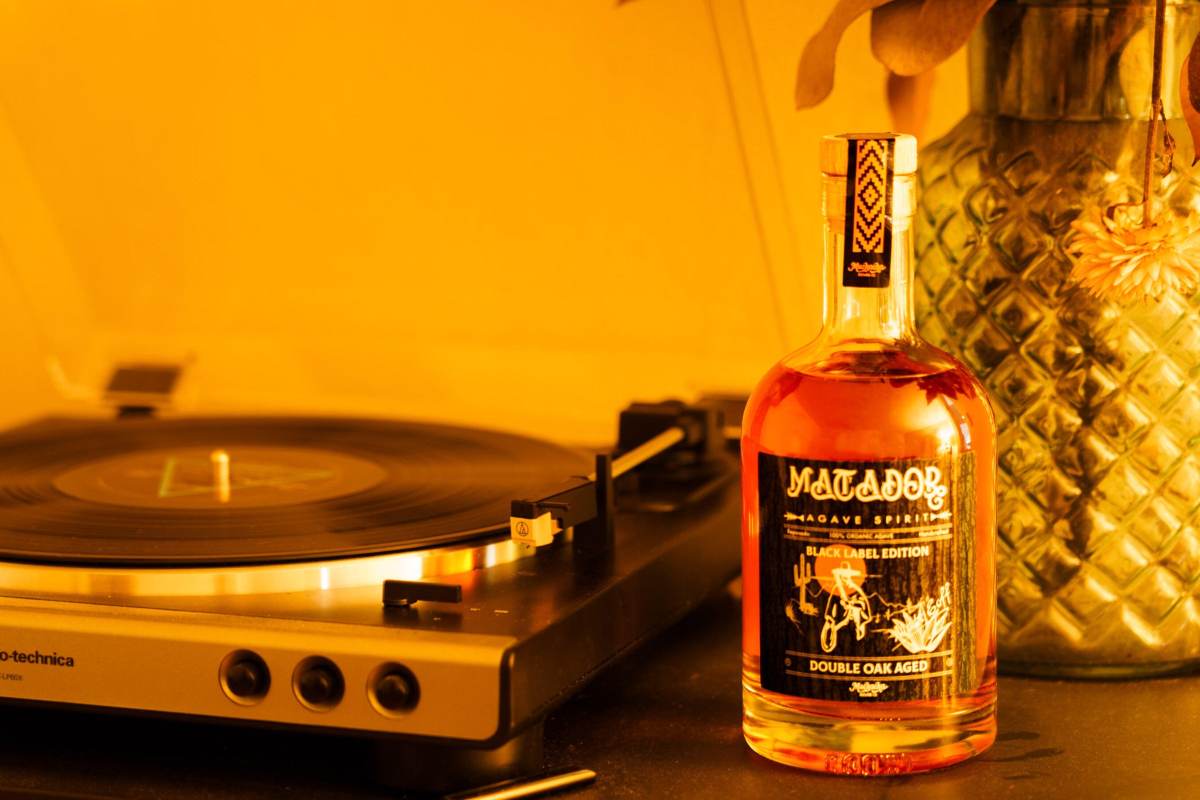 Bottle of black label tequila next to a record player with a warm yellow tint.