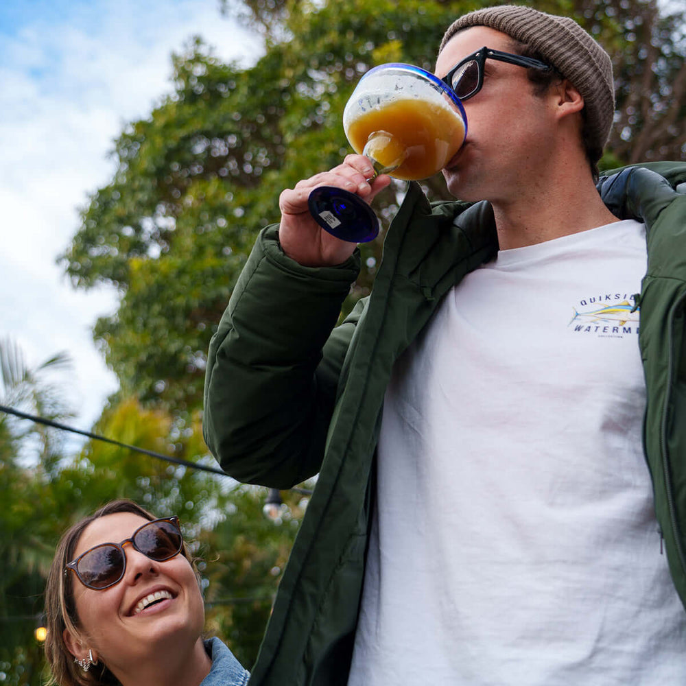 Man drinking from a mango and passionfruit margarita cocktail outdoors with a woman smiling in the background party