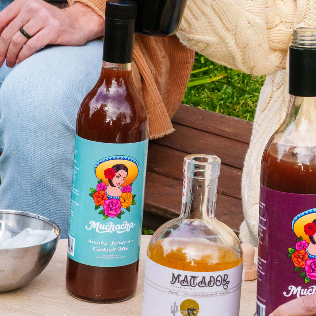 Three bottles of 'Muchacha' and 'Matador' cocktail mix on a table with a person sitting in the background.