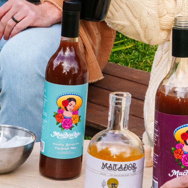 Three bottles of 'Muchacha' and 'Matador' cocktail mix on a table with a person sitting in the background.